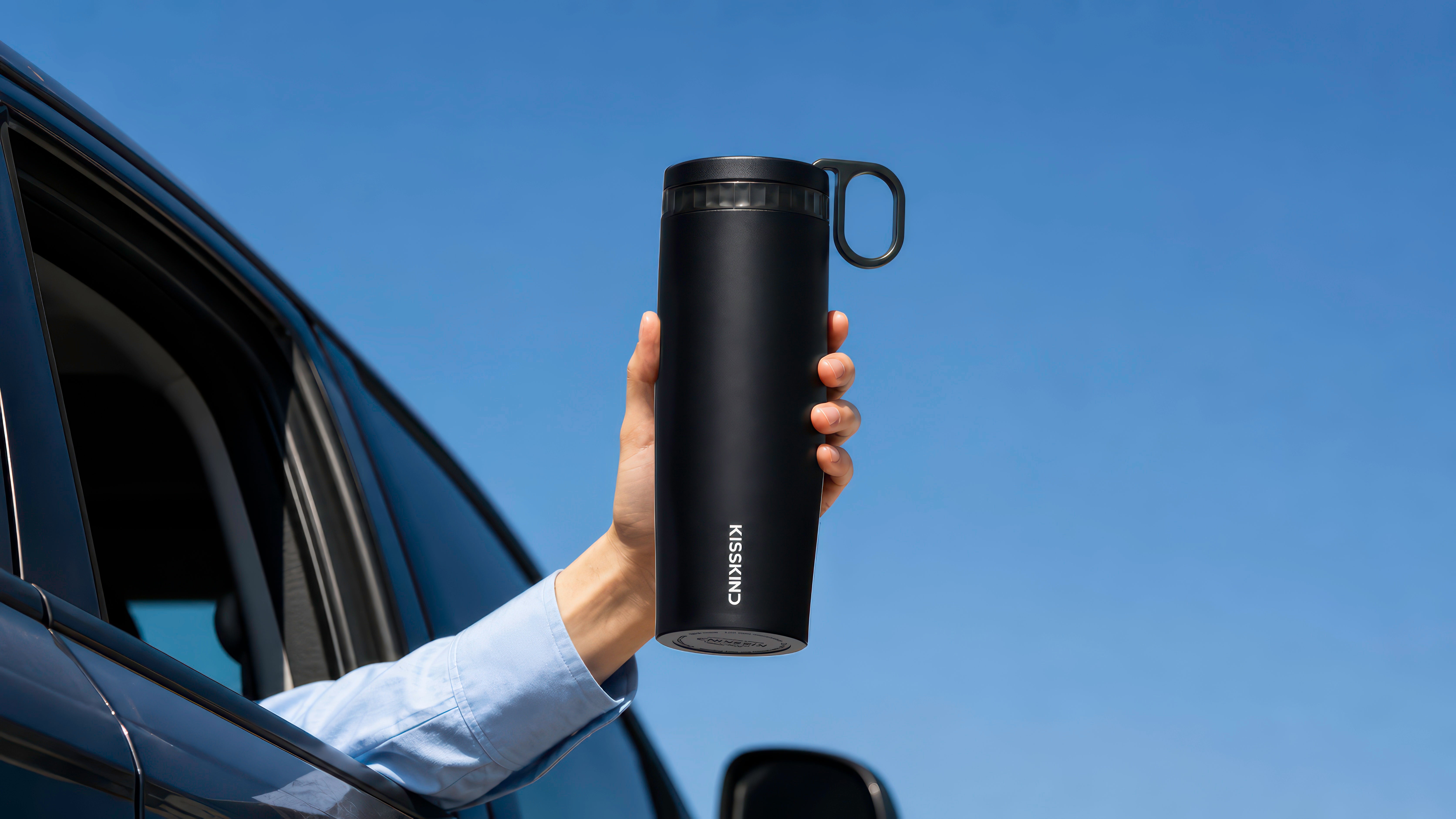 Black Kisskind cup held beside an open car window under a clear blue sky